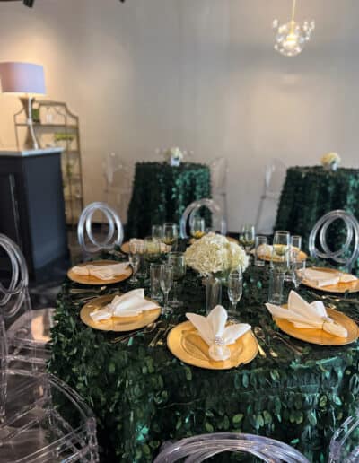 Elegant tables covered in green tablecloths, with clear acrylic chairs, in a modern room with pendant lights.