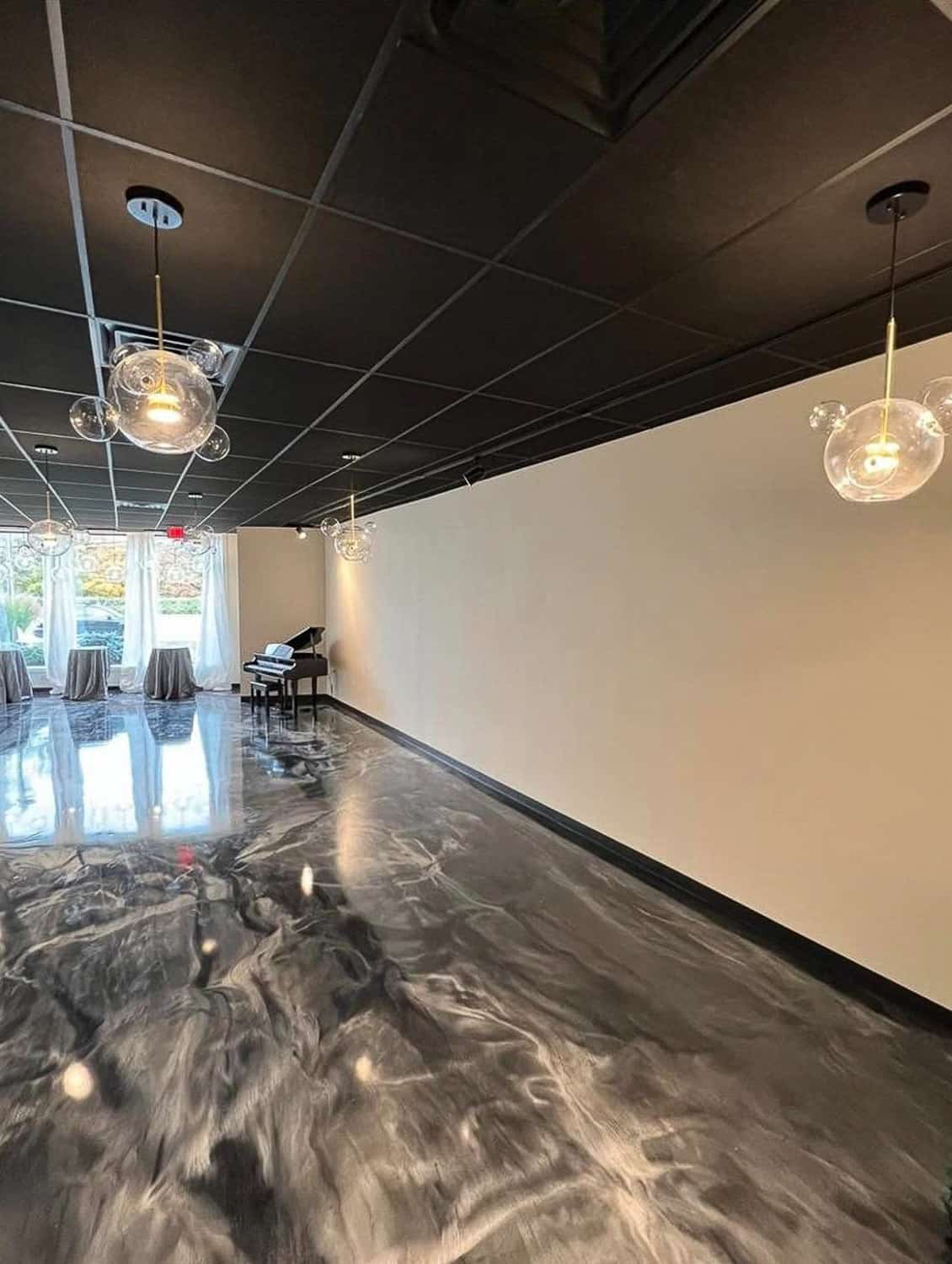 Modern interior of an event venue with marble floors, round light fixtures, and tables with chairs in the background.