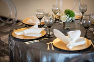 Elegant dining table with golden chargers, white napkins, and glasses, accompanied by floral centerpieces.