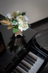 A vase with white flowers and silver ornaments on top of a glossy black piano.