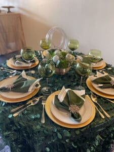 Elegant dining setup with green and gold theme, with napkins folded into leaf shapes, matching plates, and decorative greenery.