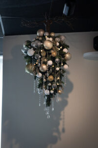 An upside-down Christmas bouquet of silver and gold ornaments, pine cones, and beads hanging from a ceiling.