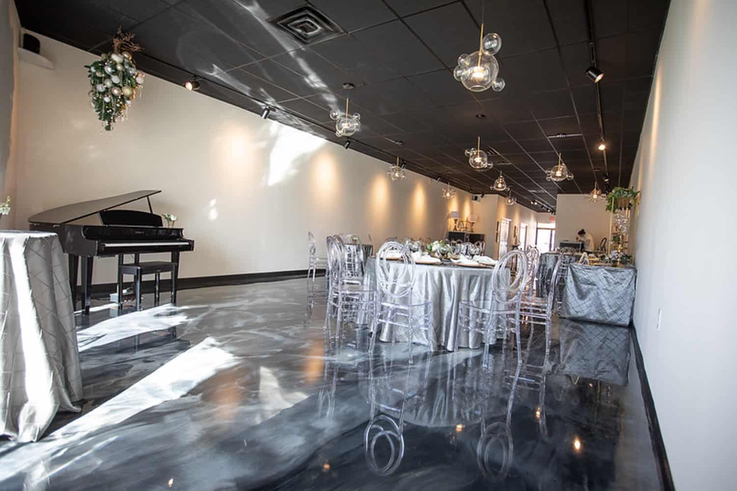 Elegant event venue interior with glossy marble floors, decorated tables, hanging glass lights, and a piano in the corner.