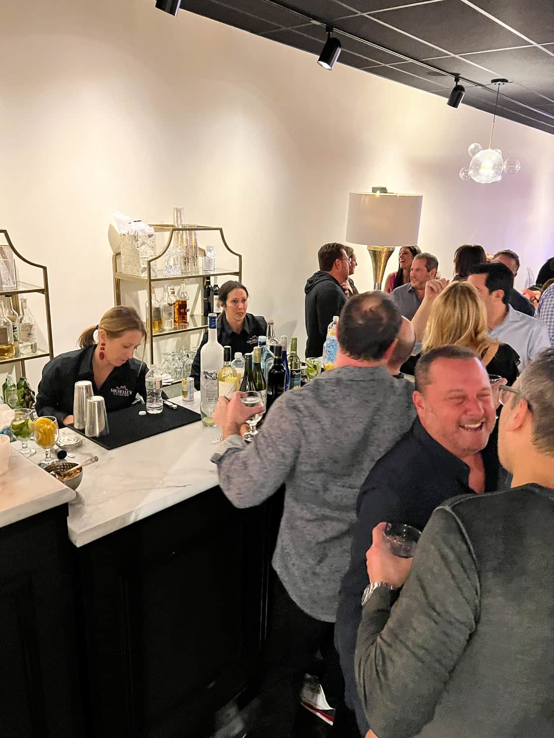 People socializing and laughing at a bar, with a bartender preparing drinks in the background.