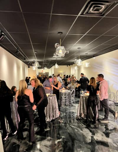 People socializing at a formal indoor event with elegant decor, featuring marble floors and modern hanging lights.