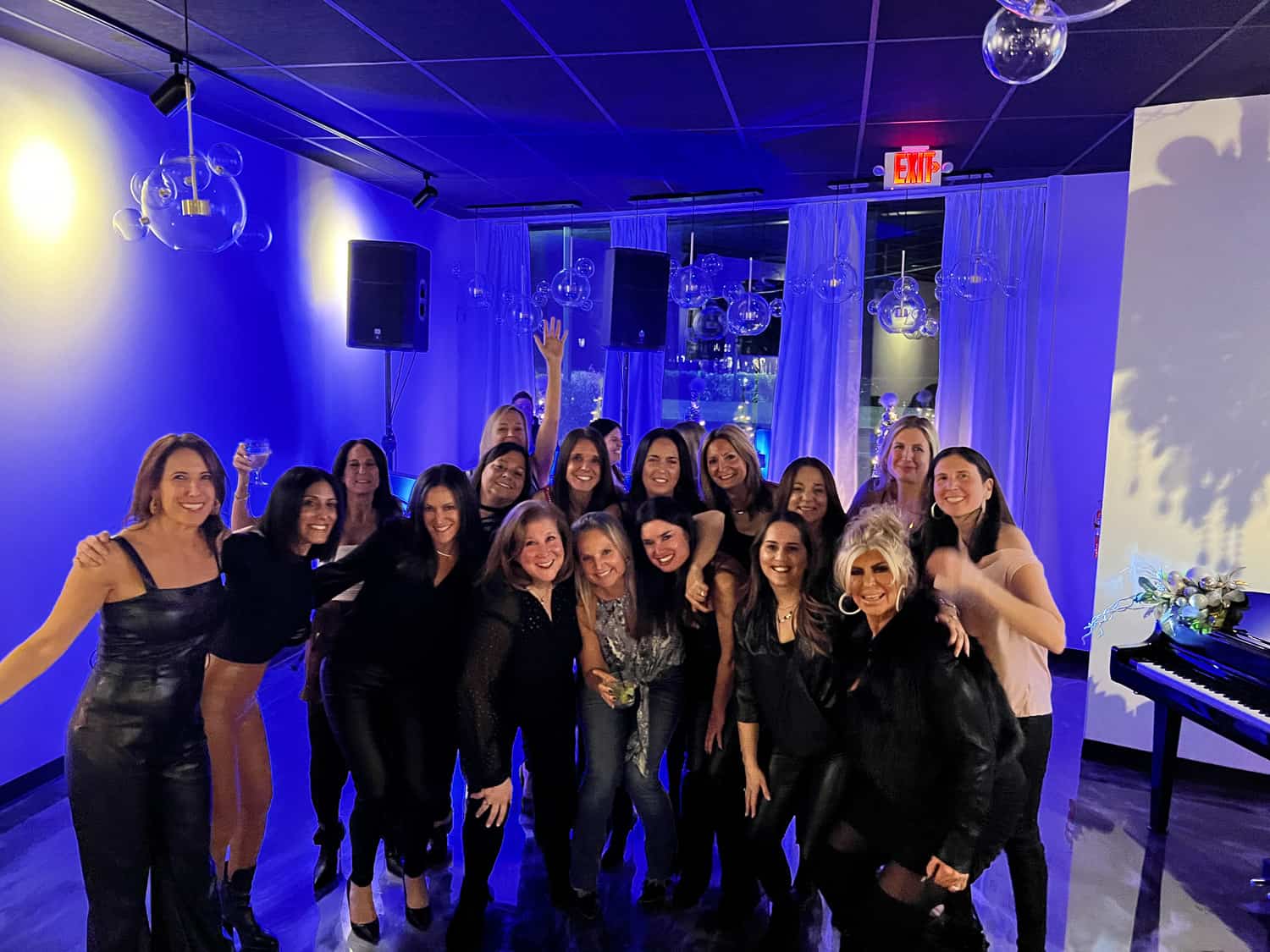 A group of happy women posing together in a room with blue lighting and modern decor during a social gathering.
