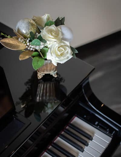 A vase with white flowers and silver ornaments on top of a glossy black piano.