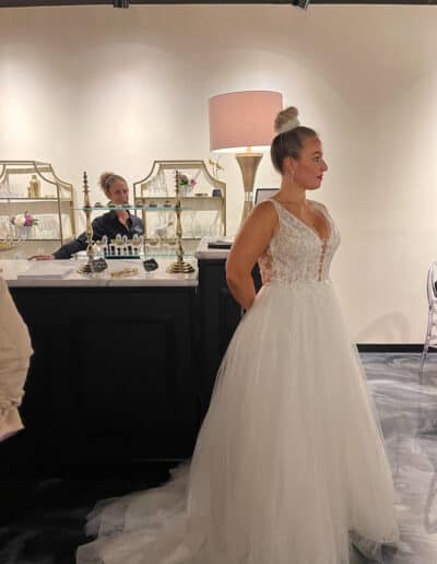 A bride in a white wedding dress stands at a reception with elegant decor, and another woman at the bar.