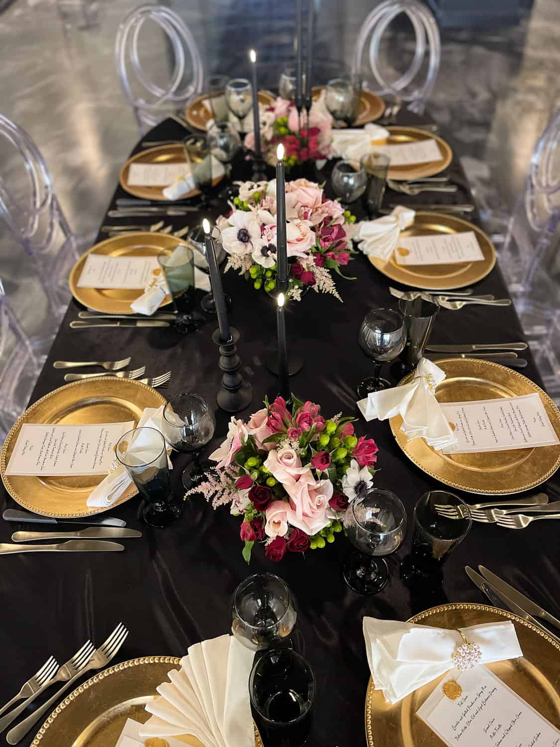 Elegant dining table set for ten with gold plates, crystal glassware, and floral centerpieces on a black tablecloth.