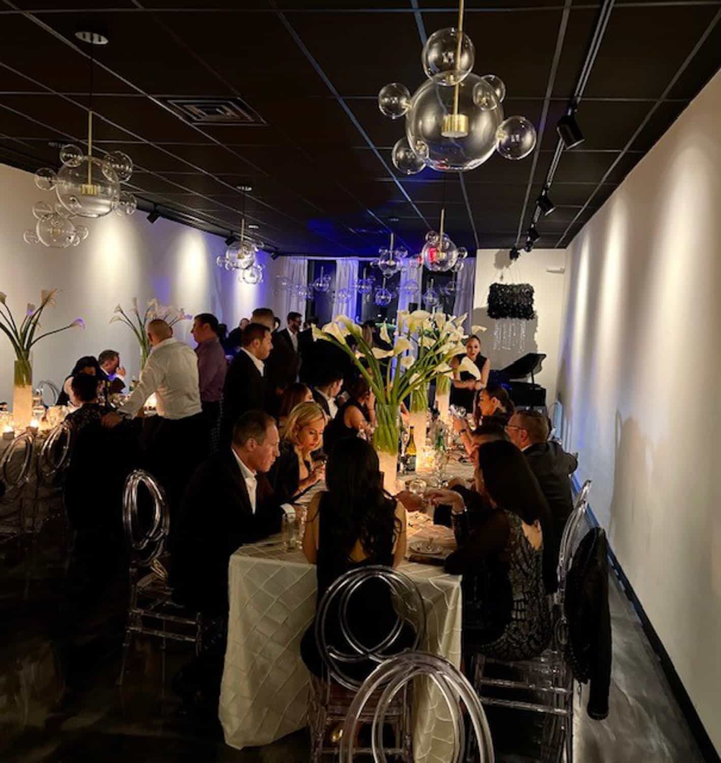 Guests seated at round tables dining in a dimly lit, elegant room with cala lily centerpieces.