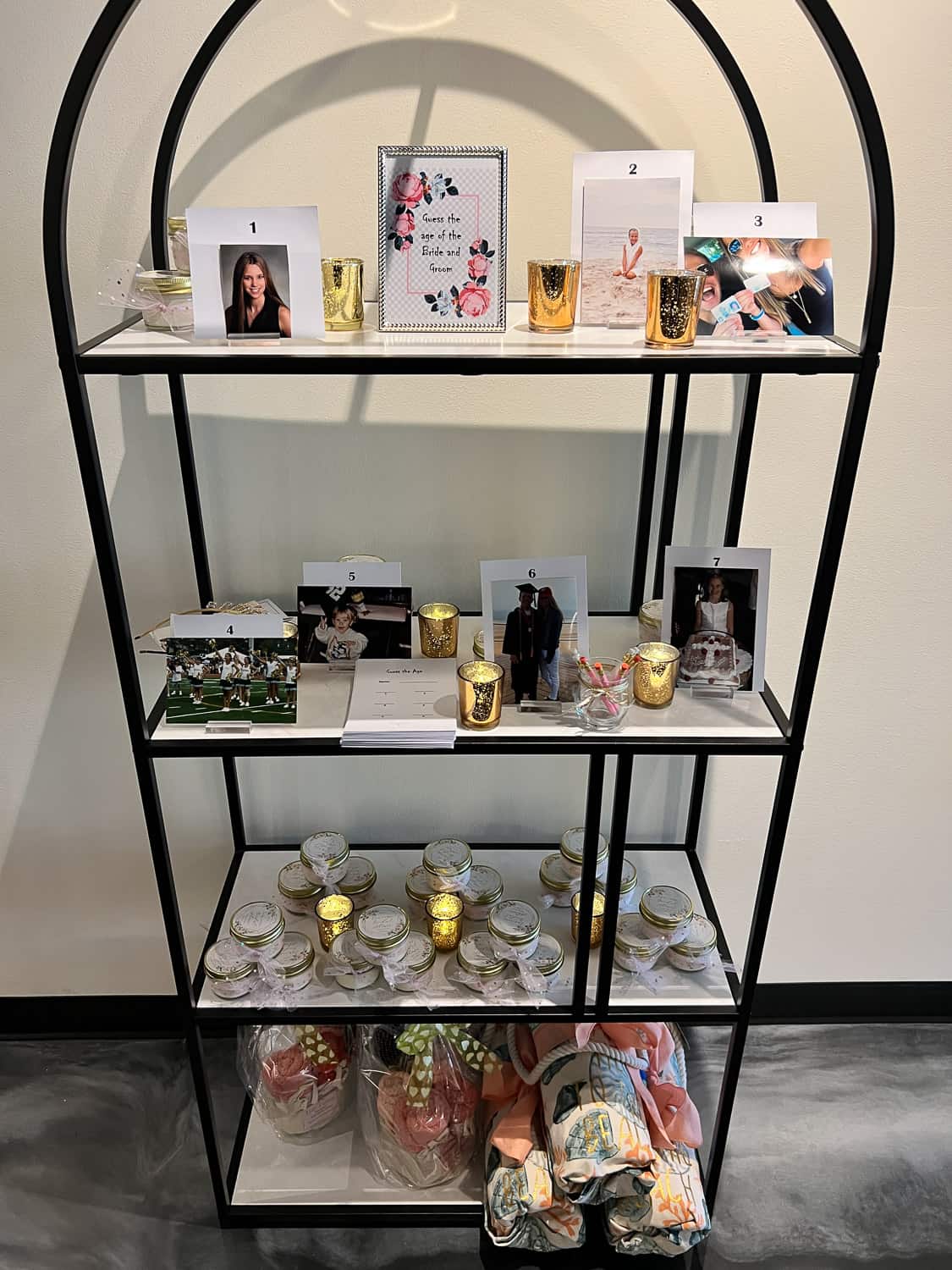 Shelf displaying various items such as framed photos, notebooks, decorative cups, candles, and fabric bundles.