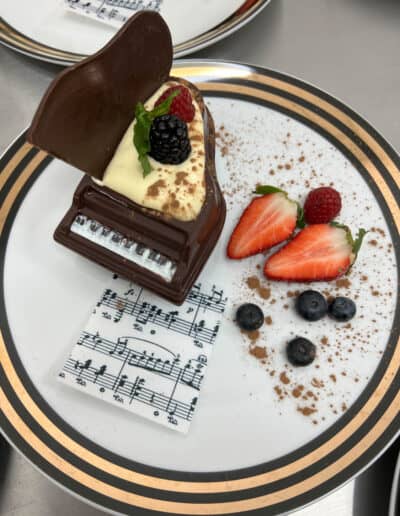 Chocolate dessert that resembles a piano, garnished with fresh berries and mint, presented on plates with musical note designs.