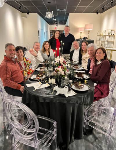 Ten people smiling at a table with elegant black and white decor, floral centerpieces, and clear chairs in an event venue.