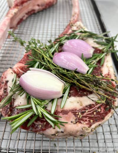 A lamp chop with rosemary and garlic on a rack on a stainless steel surface.