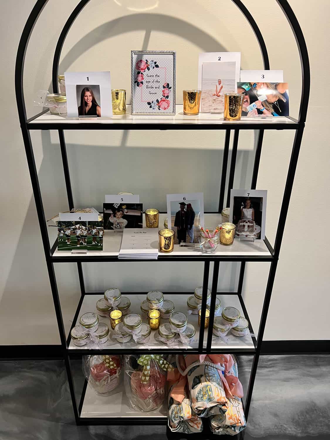 Shelf displaying various items such as framed photos, notebooks, decorative cups, candles, and fabric bundles.