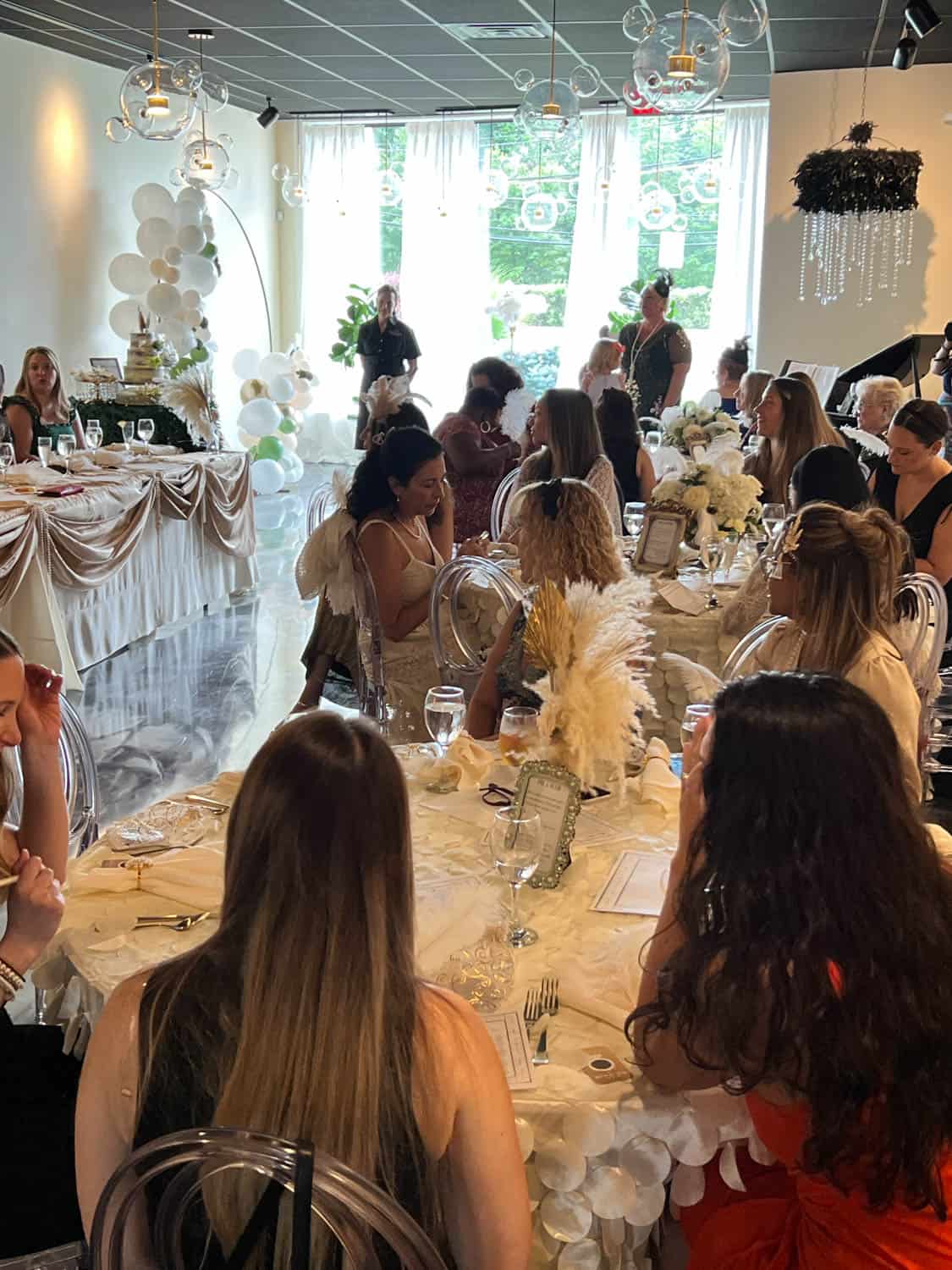 Guests seated at elaborately decorated tables during a wedding reception inside a well-lit venue with large windows.