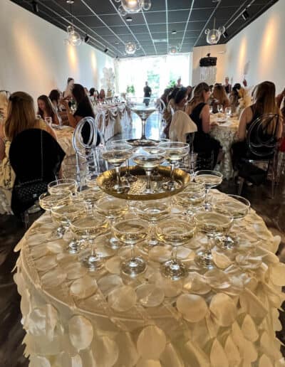 Table with champagne glasses set in the foreground at a wedding reception venue, with guests seated at tables in background.